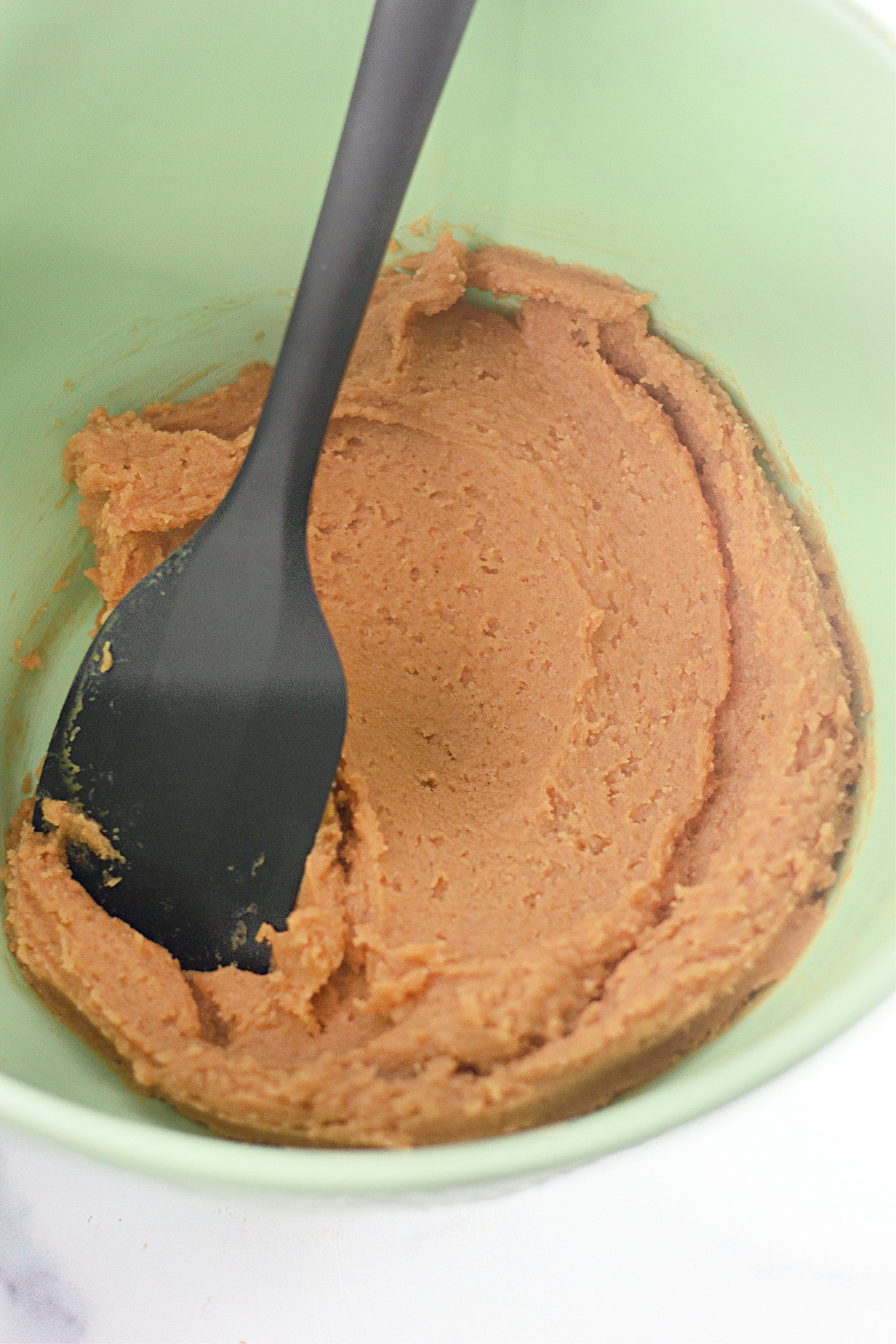 Raw peanut butter cookie batter in a green bowl with a large black spoon.