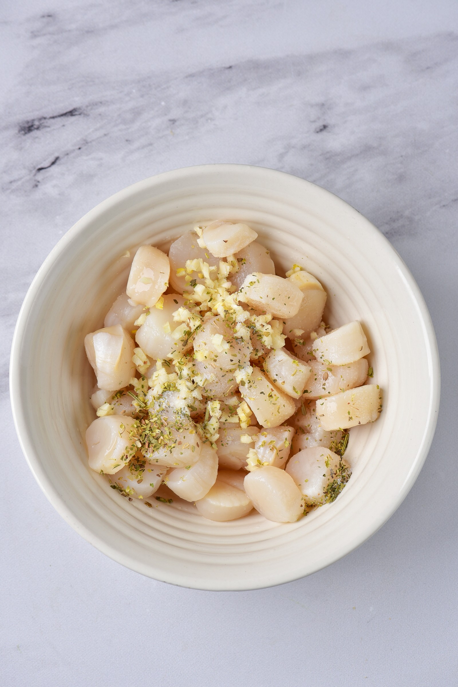A white bowl with raw scallops with seasoning.
