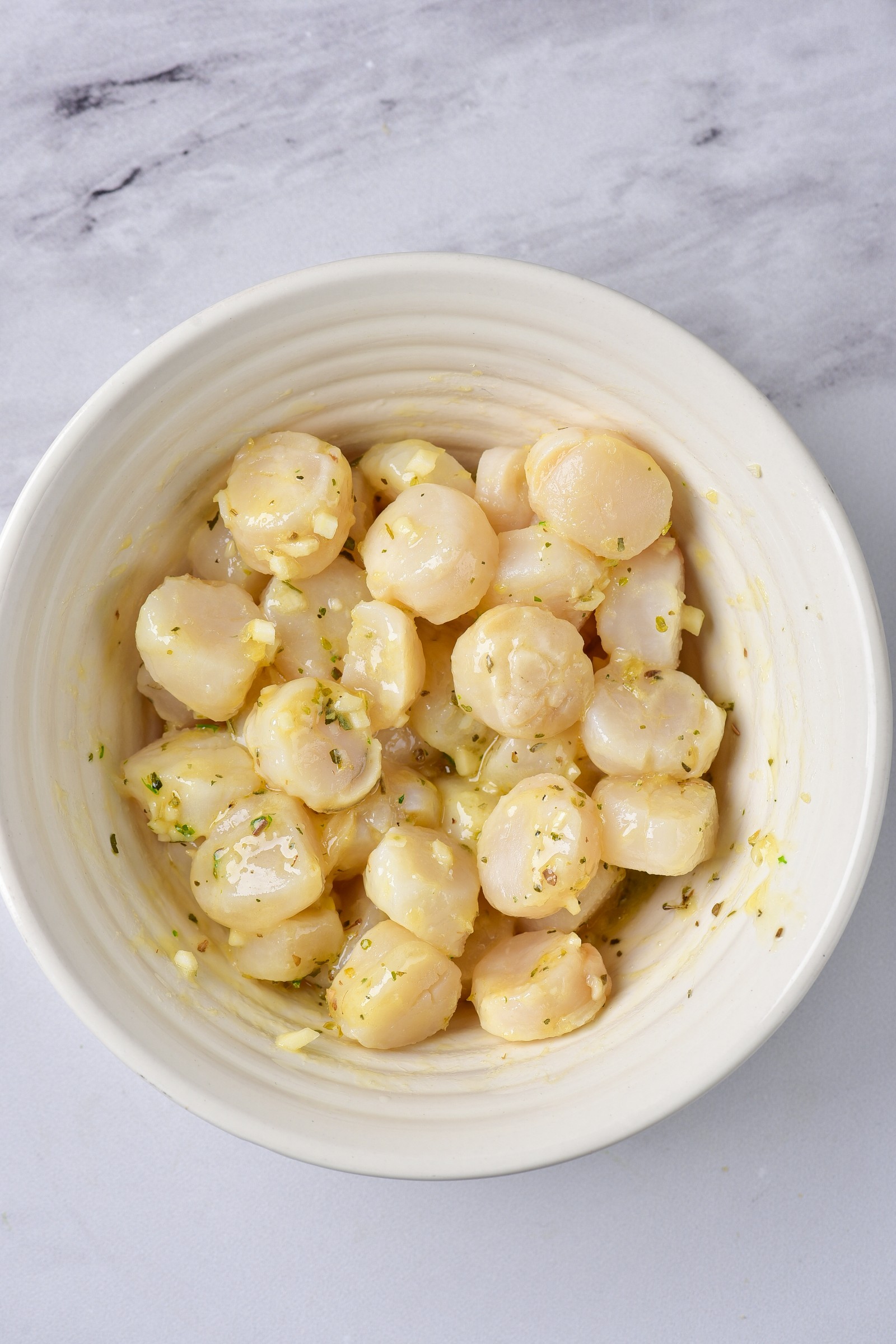 A white bowl with raw scallops with seasoning.