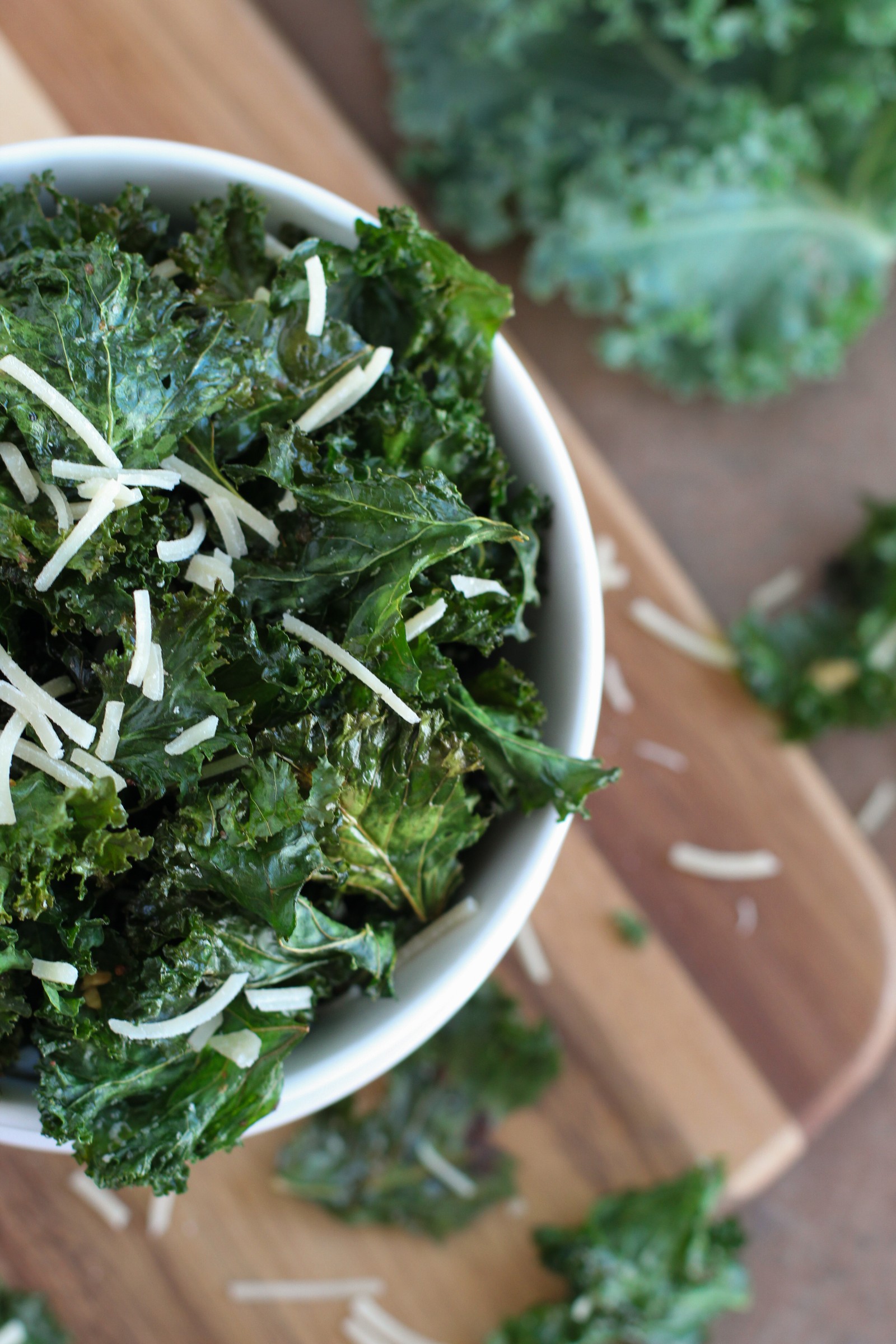 A white bowl with crispy garlicky kale chips covered in Parmesan cheese.