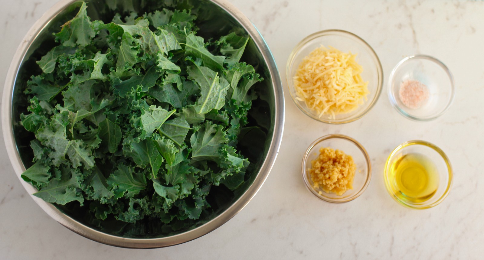 A bowl of raw kale and Parmesan cheese, minced garlic, salt, and oil.