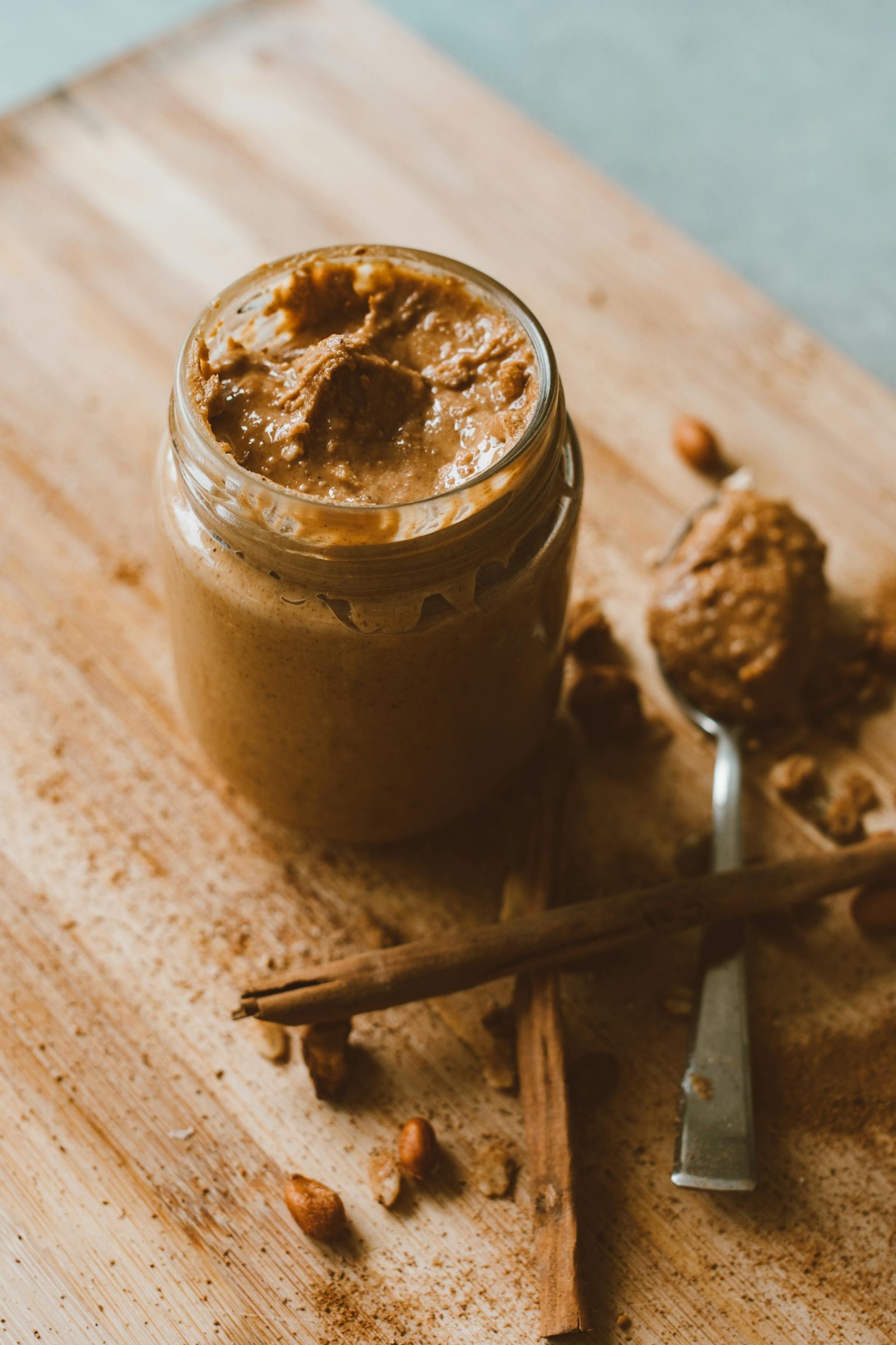 A glass jar of peanut butter with a spoon with peanut butter.