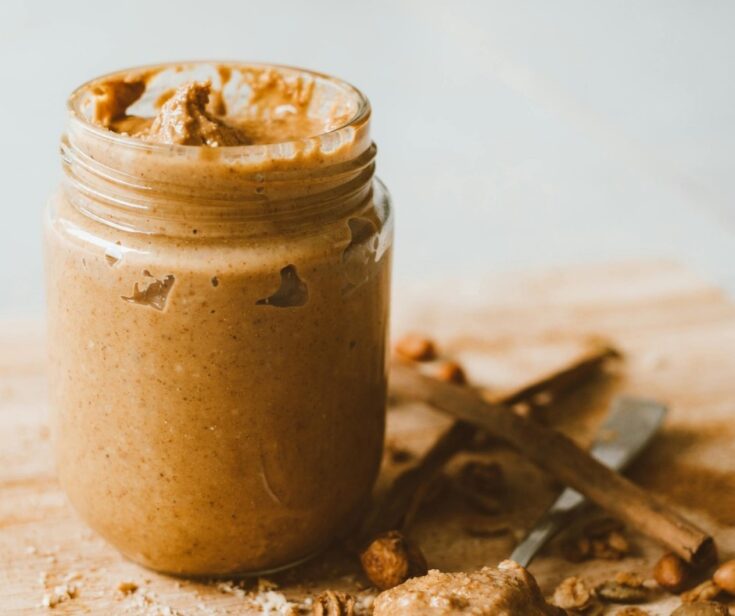 A glass jar filled with homemade peanut butter and a spoon with peanut butter on it.