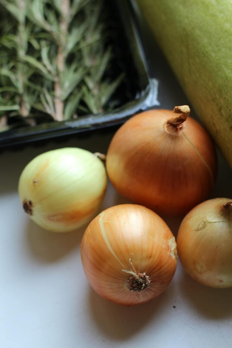 Four onions beside a box of rosemary on a kitchen counter.
