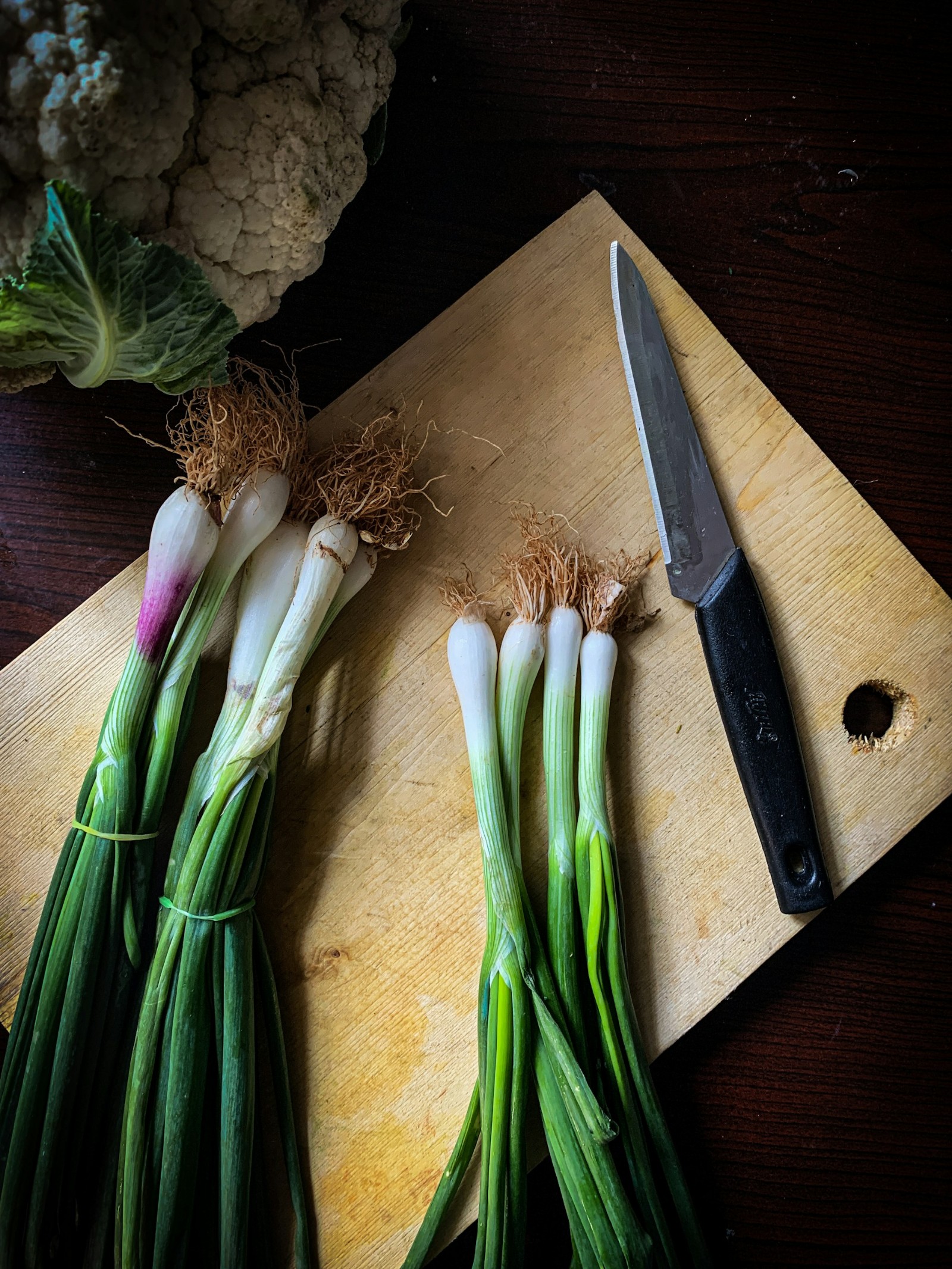 Spring onions on a cutting board with a knife.