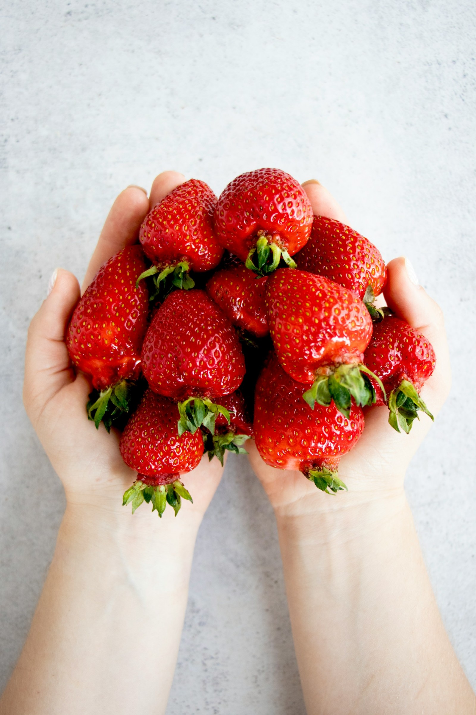 A woman's hands holding a pile of strawberries.