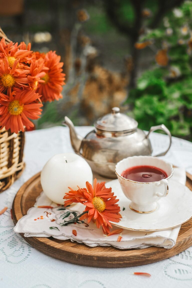 A tea cup, a tea pot, and flowers outside.