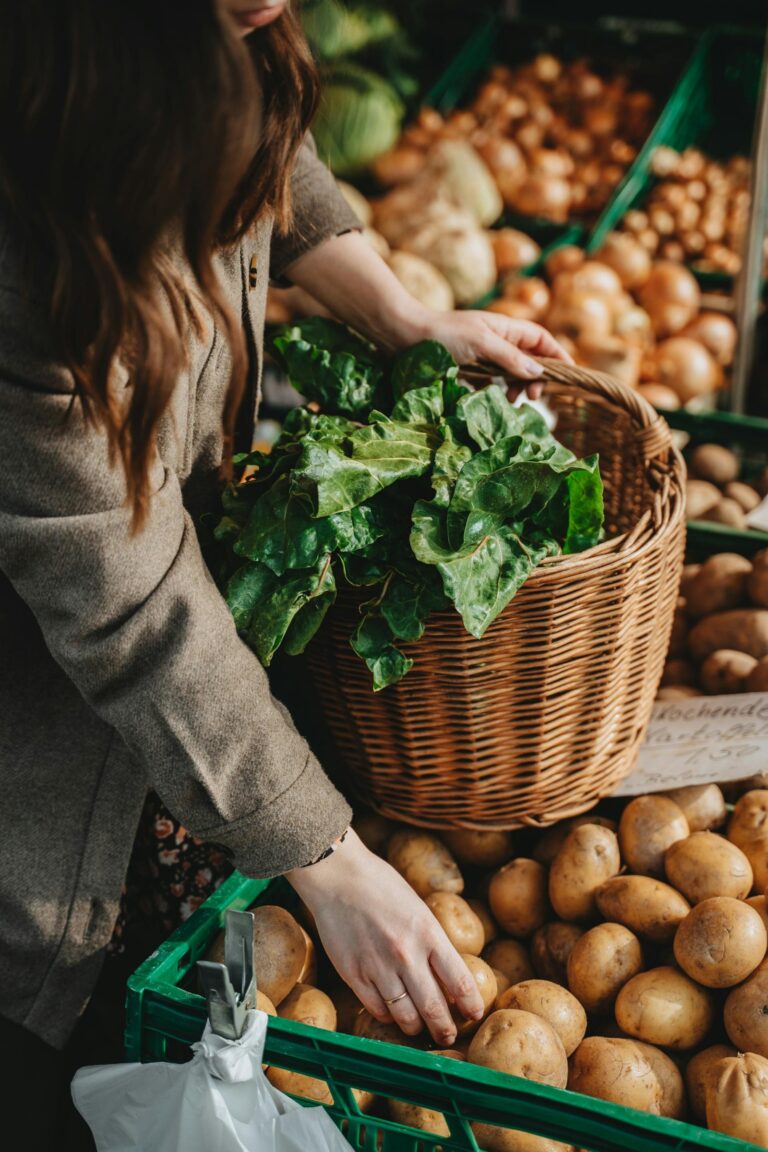 A woman is shopping for potatoes at a farmer's market with a basket.