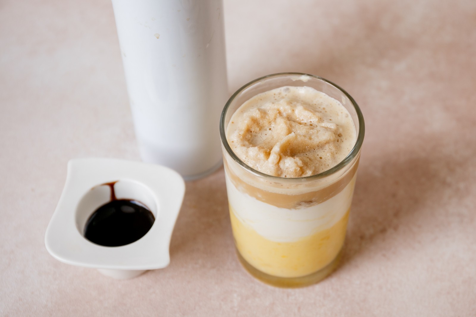 A glass filled with a layer of blended banana, whipped heavy cream, and coffee blended with ice.