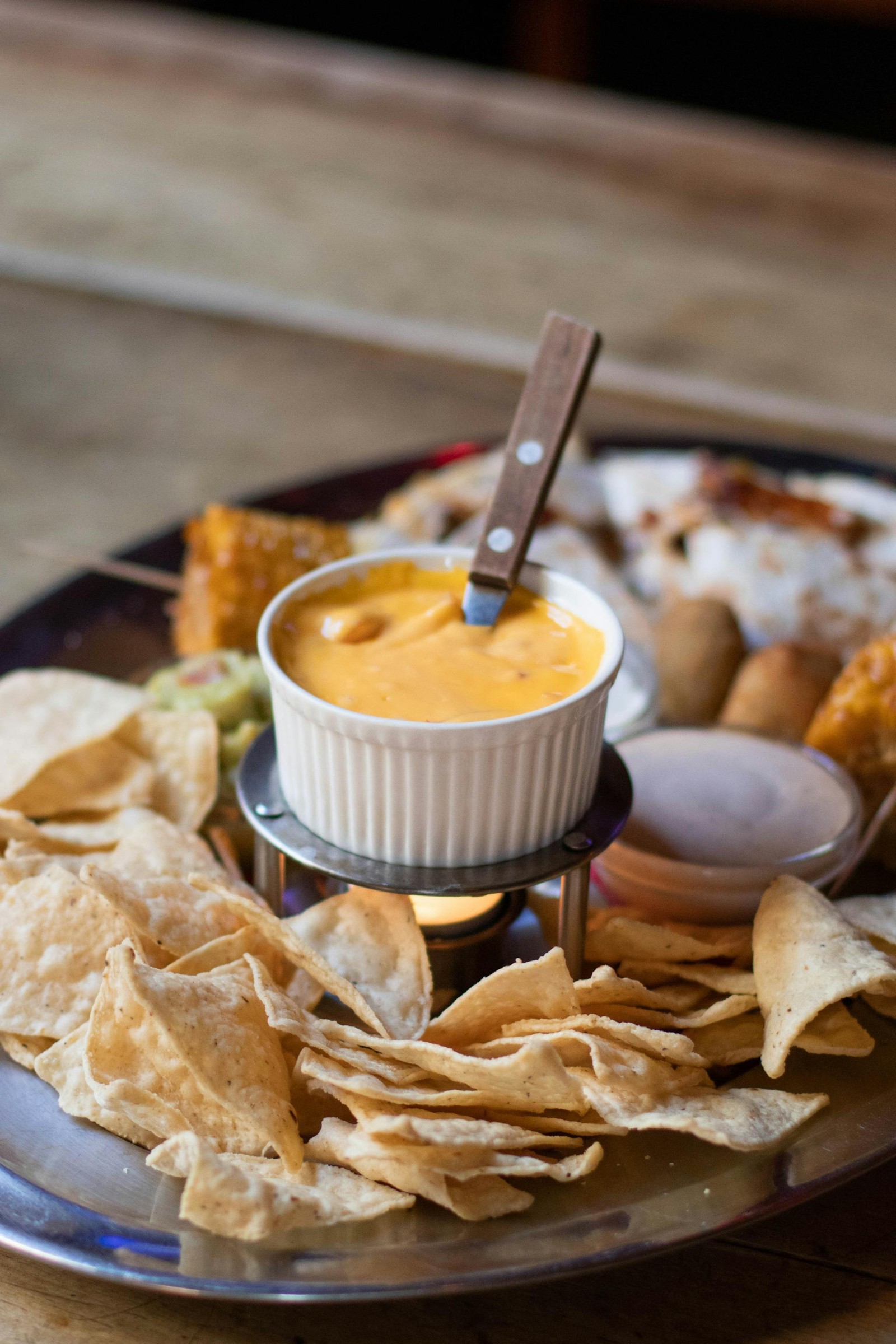 Cheese sauce in a ramekin over a little candle with a platter of tortilla chips and other appetizers.