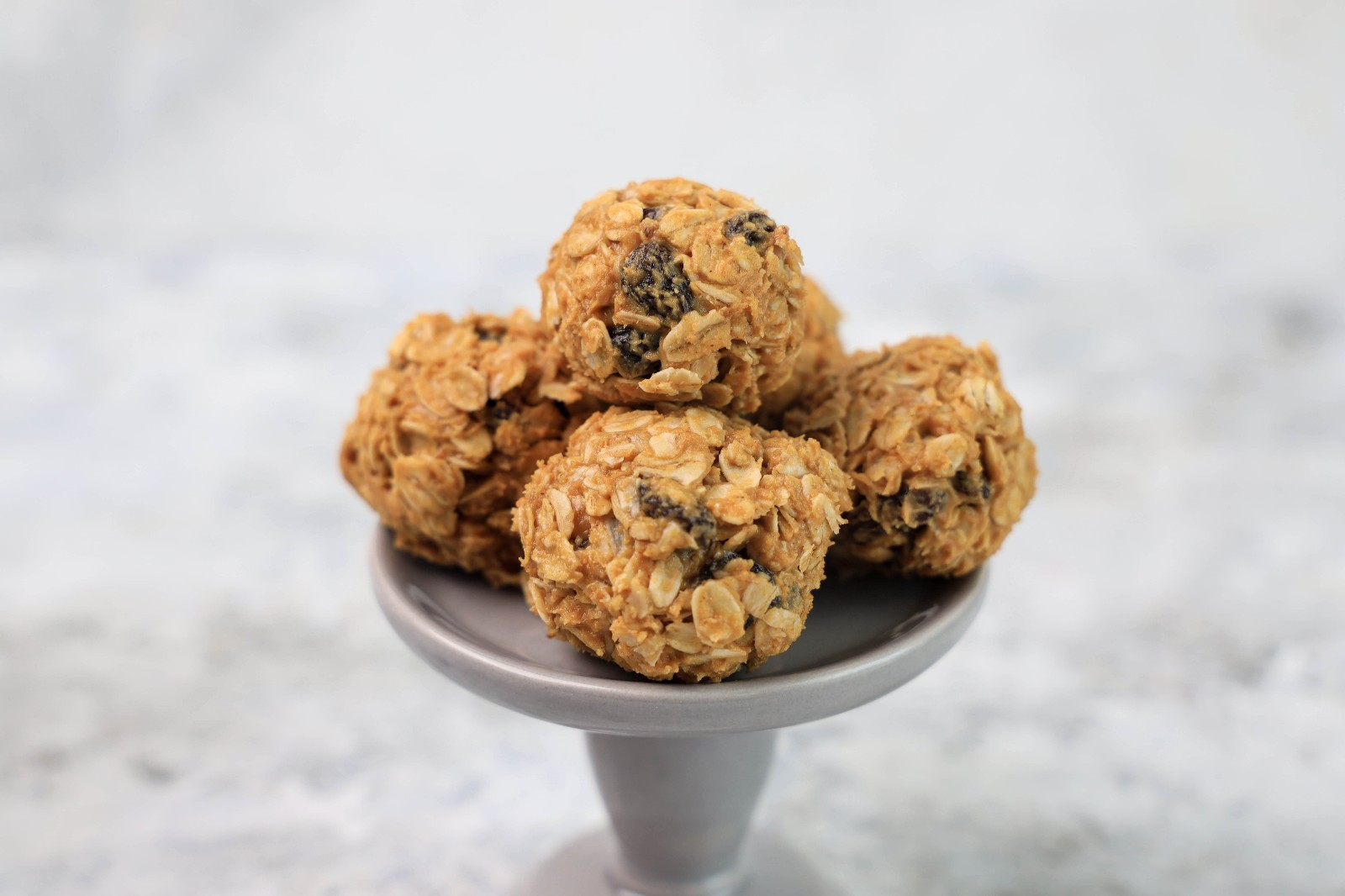 A grey dessert stand with a couple of oatmeal raisin balls.