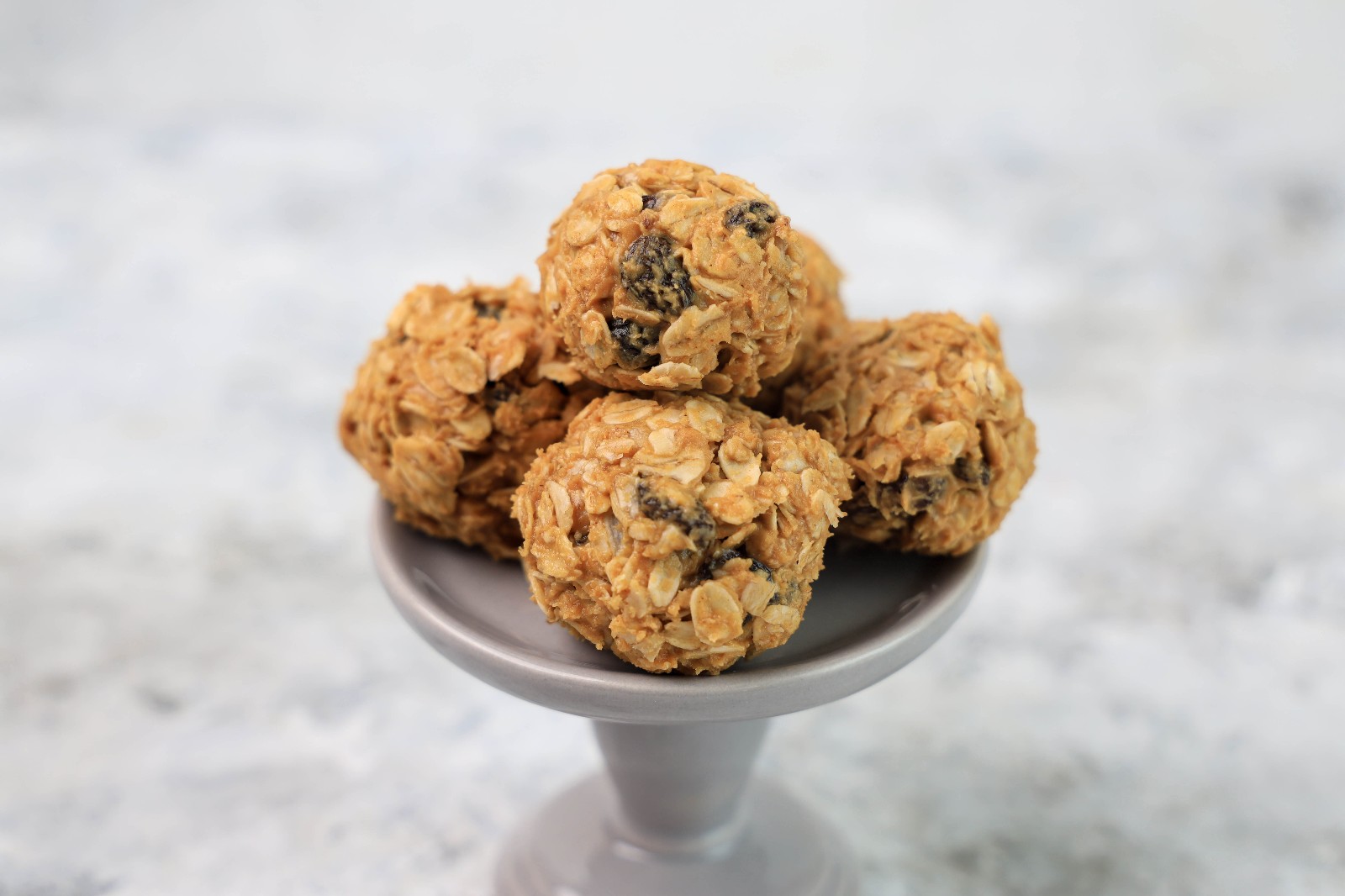 A grey dessert stand with a couple of oatmeal raisin balls.