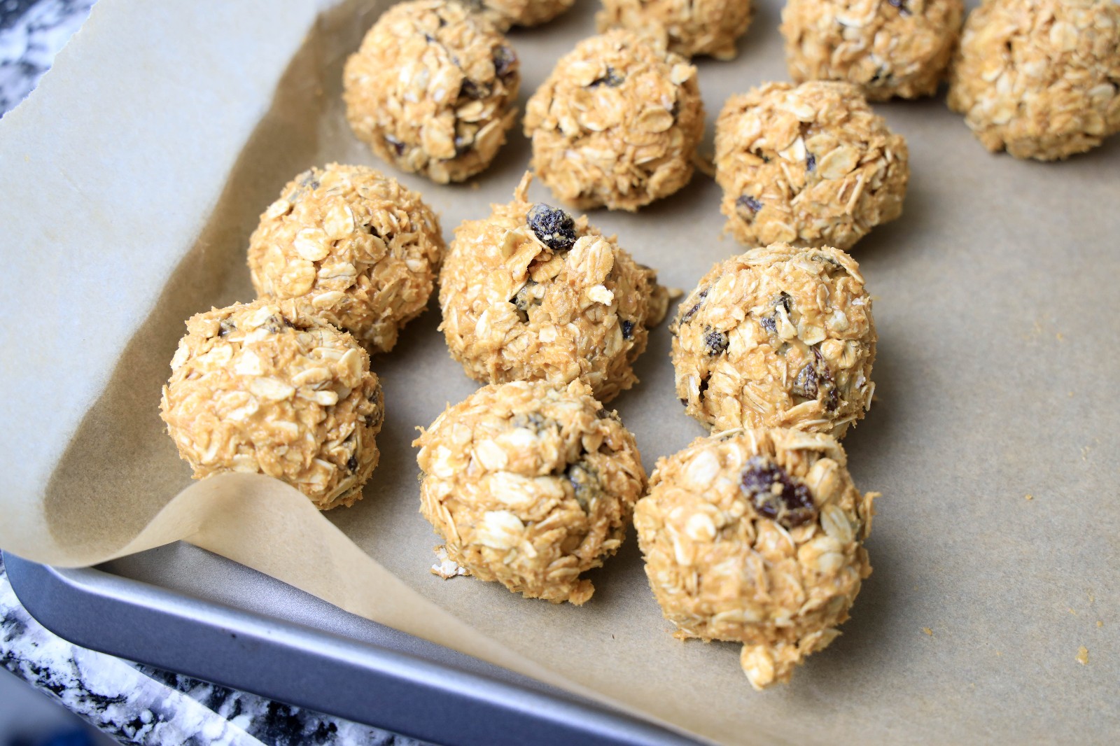 A baking sheet with 12 oatmeal raisin balls on it.