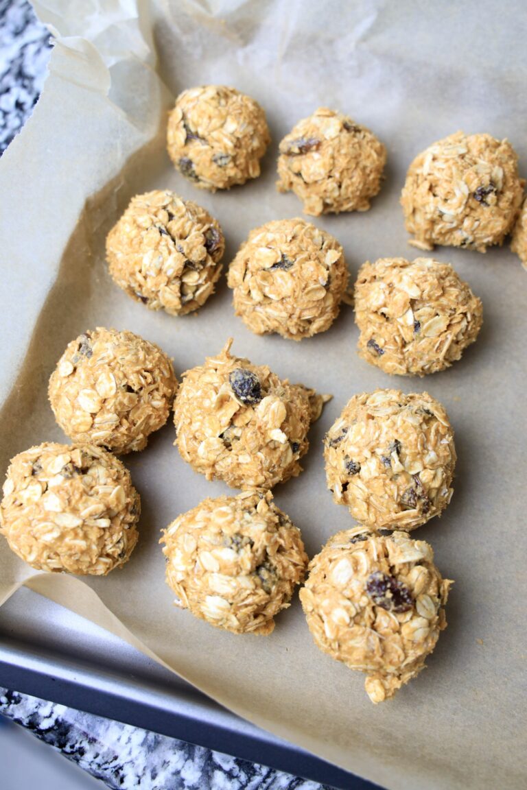 A baking sheet with 12 oatmeal raisin balls on it.