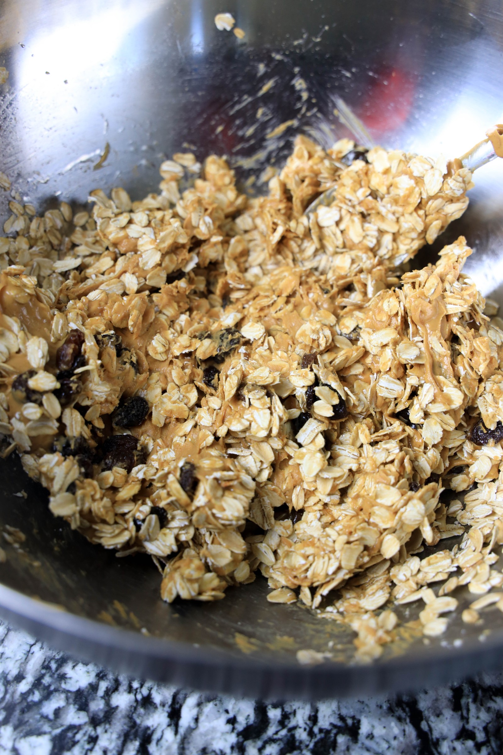 A stainless steel mixing bowl with oatmeal mixed with raisins, honey, and peanut butter.