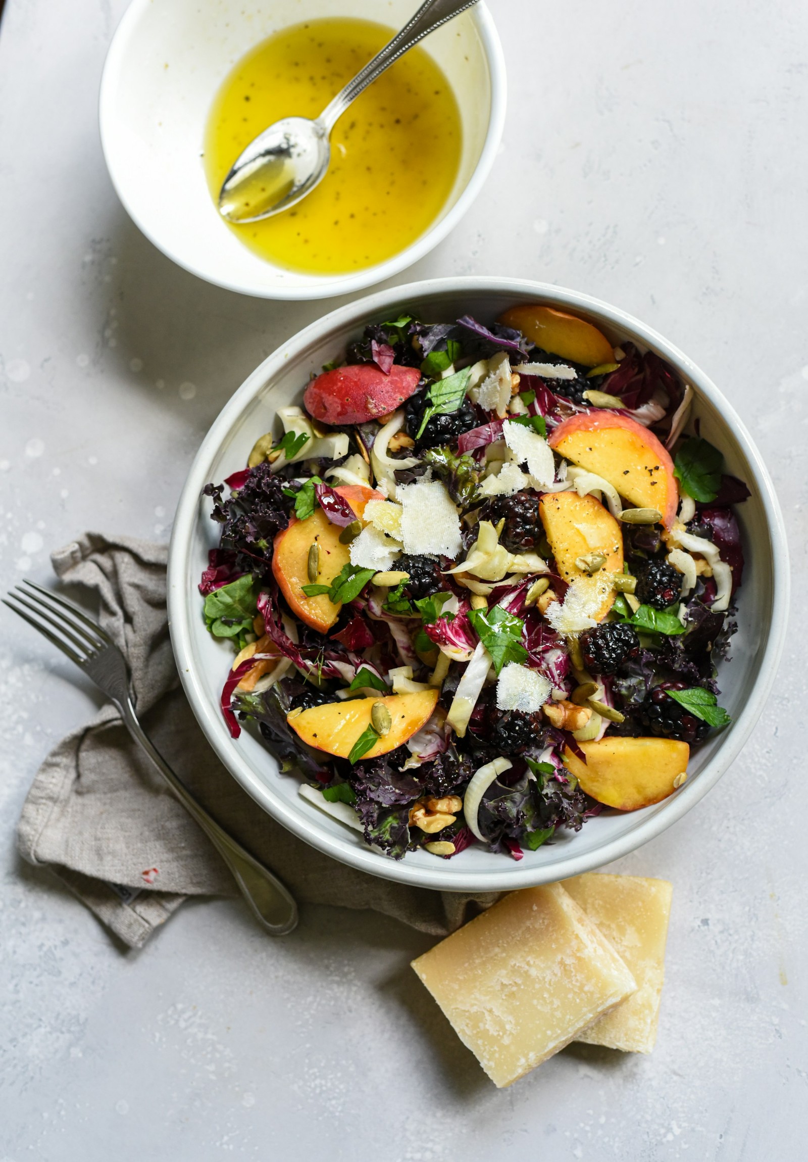A white bowl with a peach salad, some cheese, and a bowl of salad dressing.