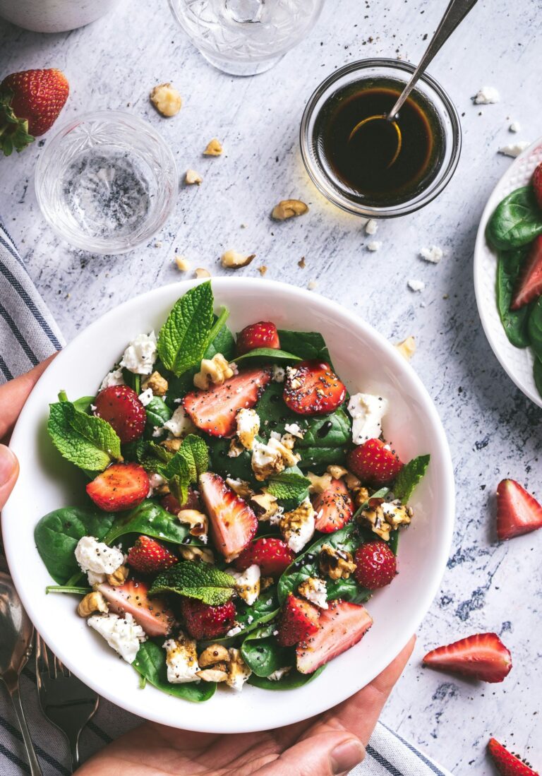 A white bowl with a strawberry salad and dressing in a jar with a spoon.