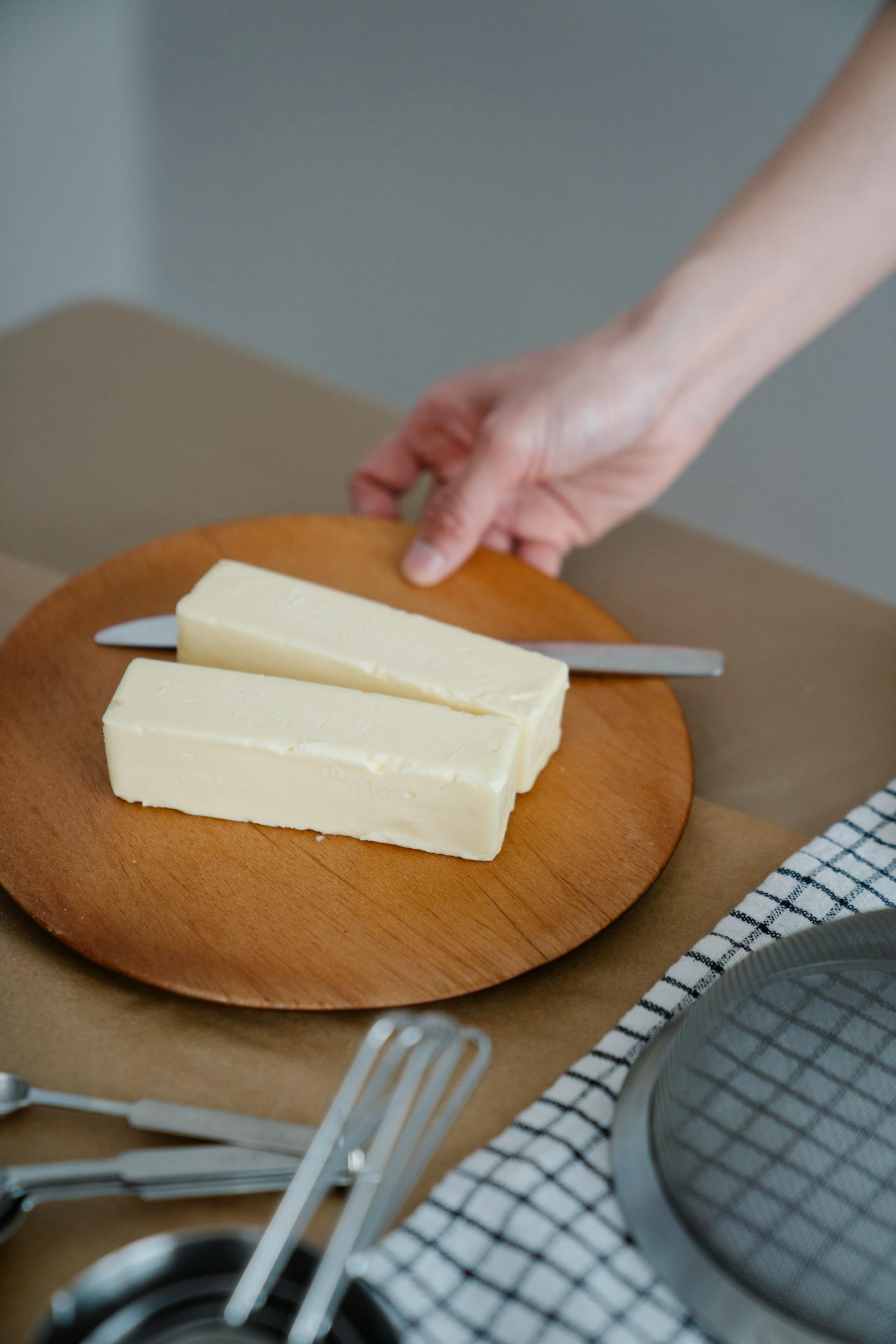 Two sticks of butter on a wooden platter with a knife.