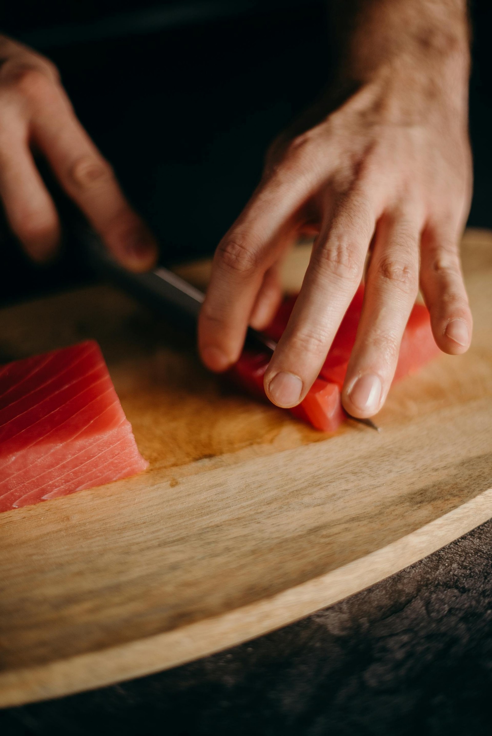 A man cutting tuna on a wooden cutting board.
