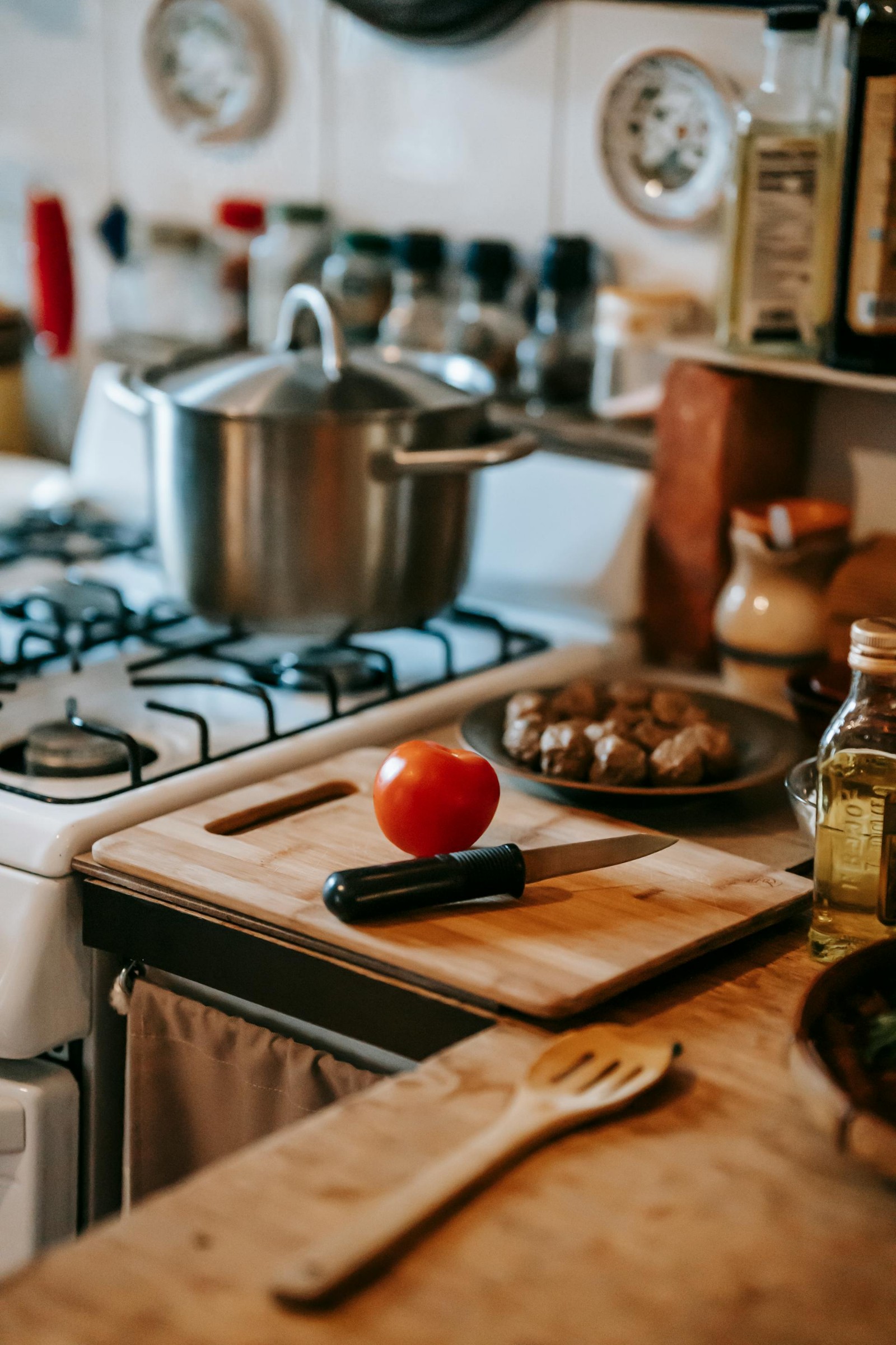 A wooden cutting board with a tomato and a knife on a kitchen counter with a white stove.