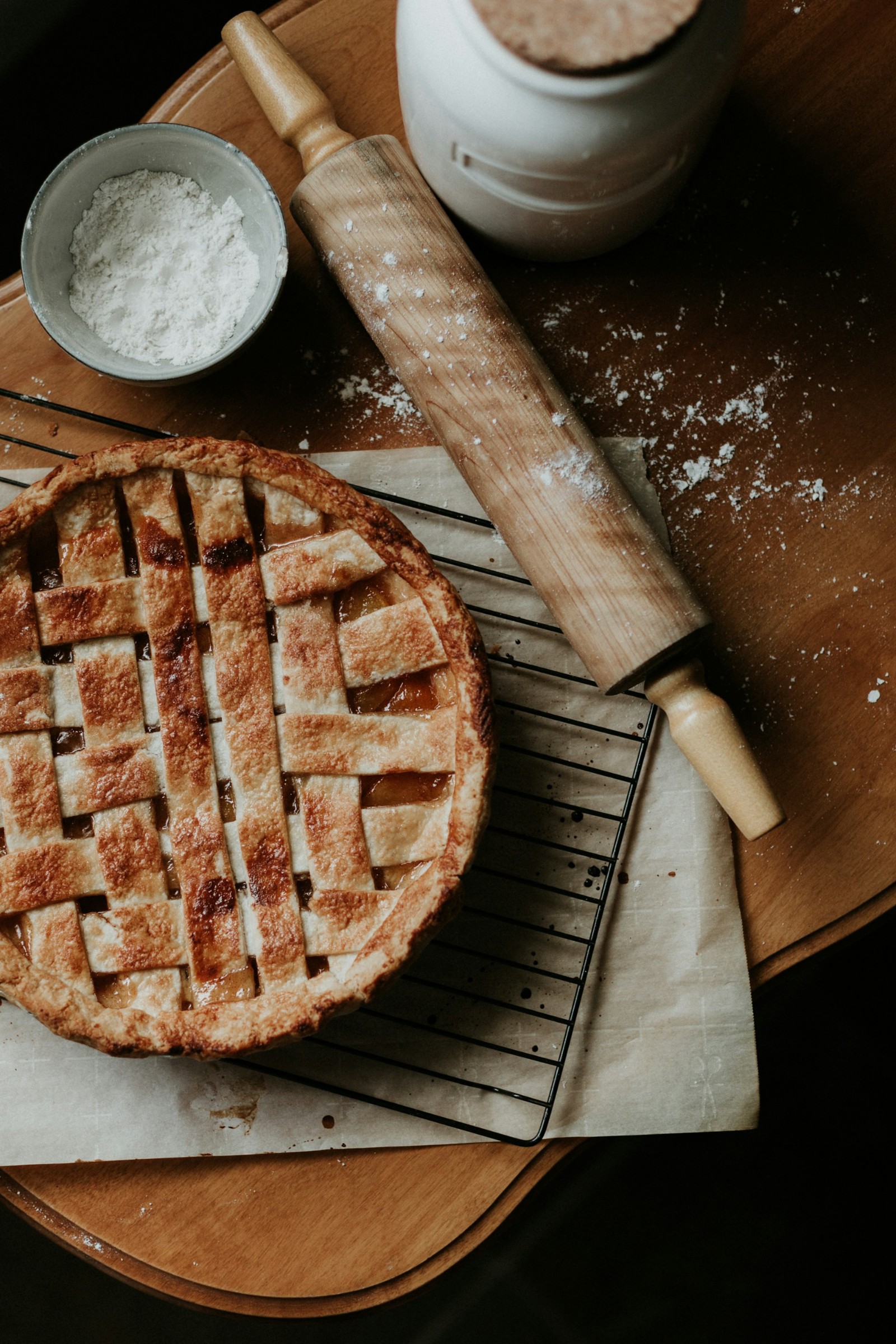 A peach pie on a cooling rack with flour and a rolling pin.