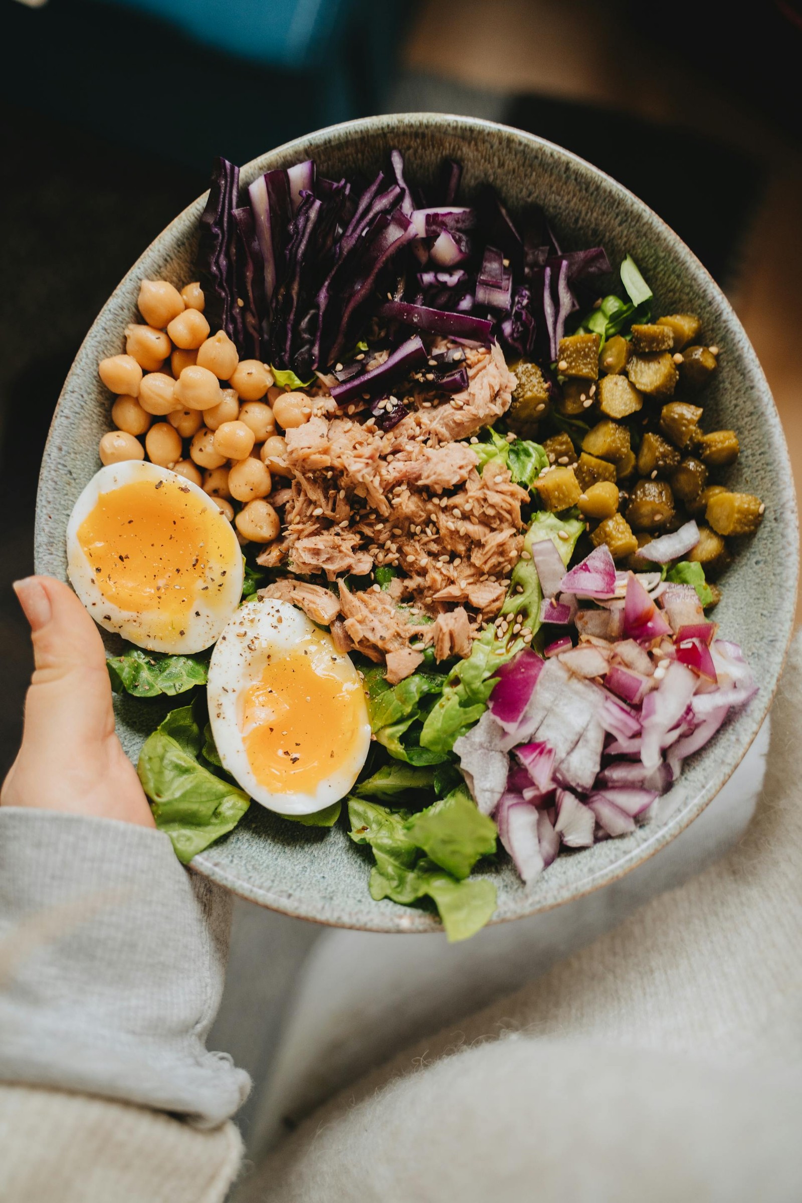 A bowl of salad with a boiled egg sliced in half, lettuce, chickpeas, onions, and tuna.