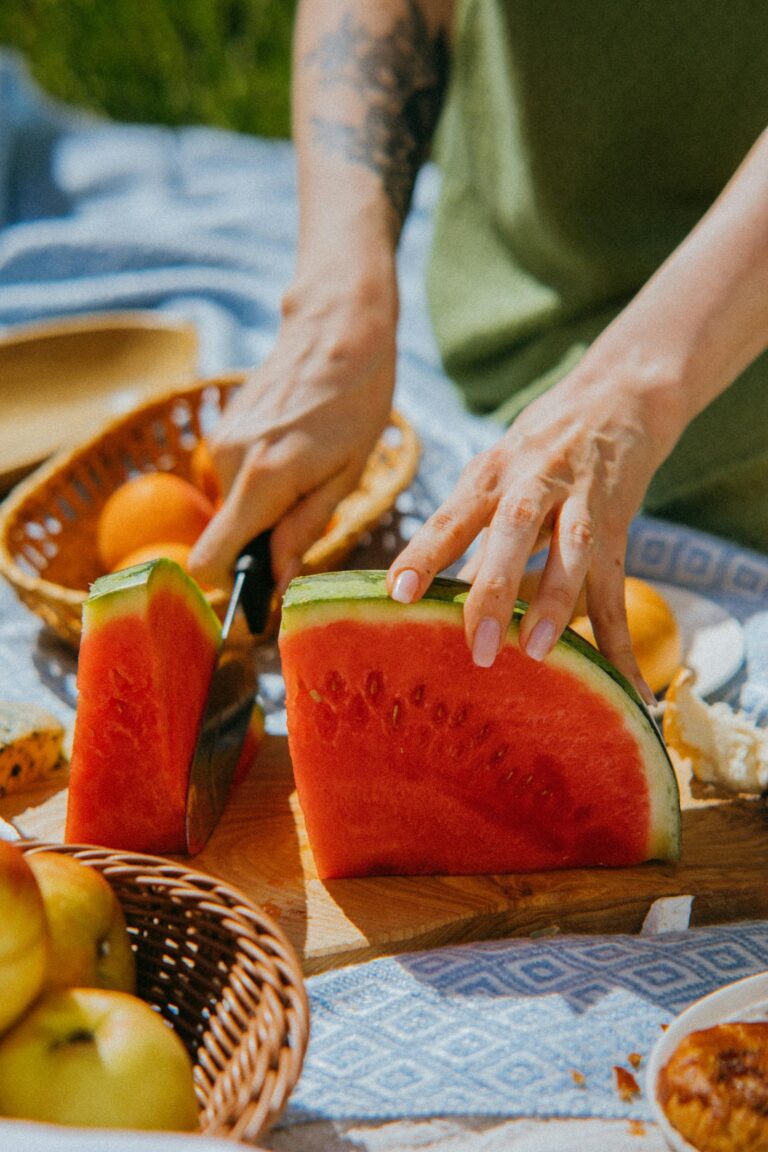 A woman's hand are shown slicing a watermelon outside.