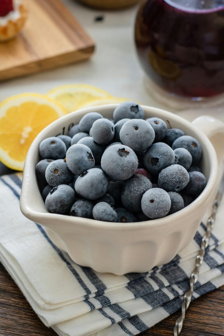 A white bowl filled with frozen blueberries and lemon slices in the background.