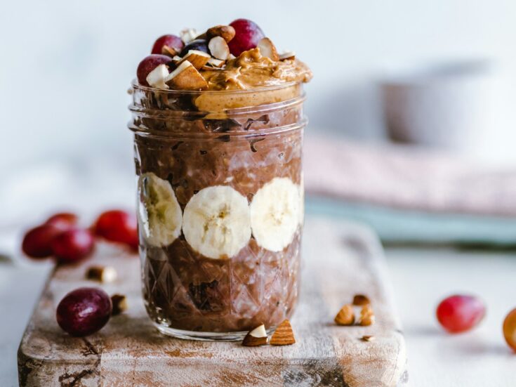 A glass jar with chocolate overnight oats on a wooden cutting board.