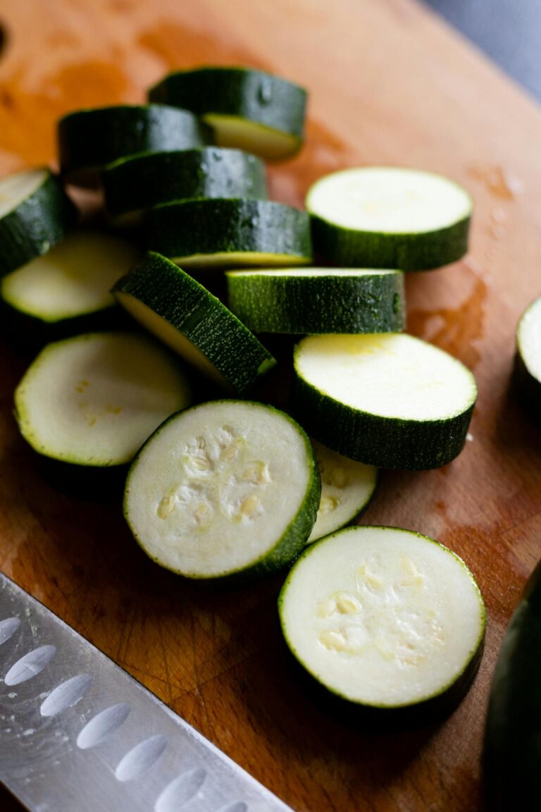 A knife beside sliced zucchini on a wooden cutting board.