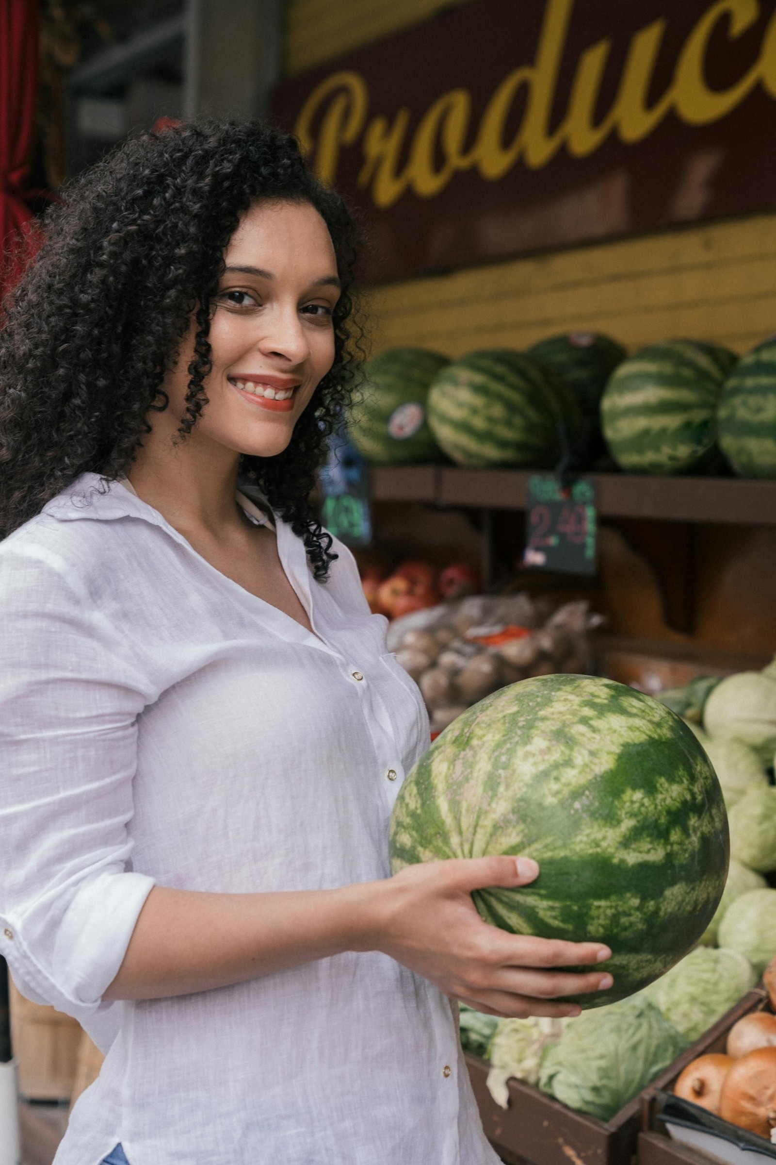 A woman holding a watermelon at a farmer's market.