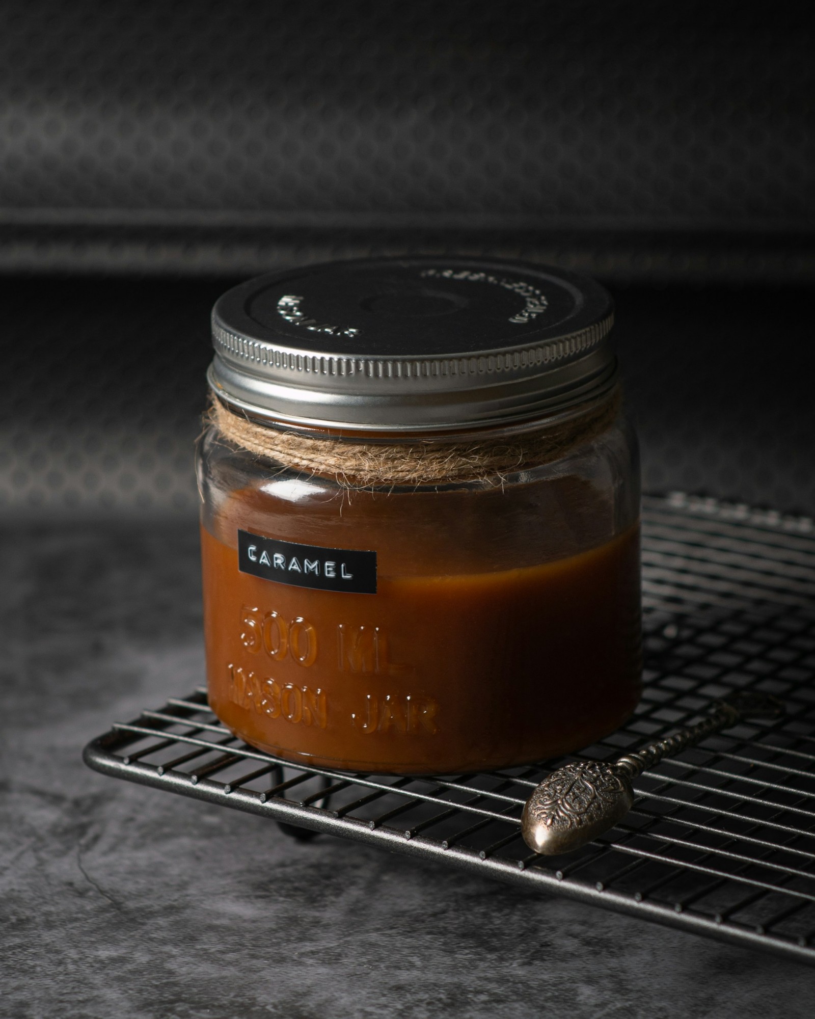 A glass jar filled with caramel sauce on a cooling rack.