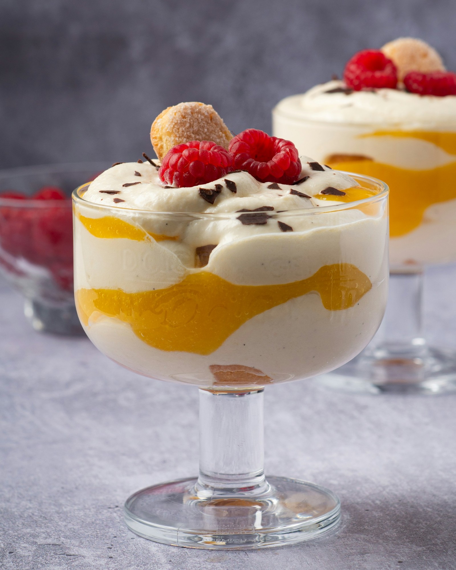 A glass cup filled with mango puree and cheesecake filling. 