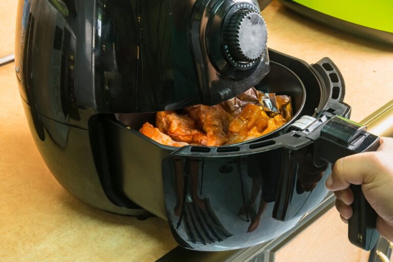 A black air fryer that is filled with BBQ chicken and a hand is pulling the basket.