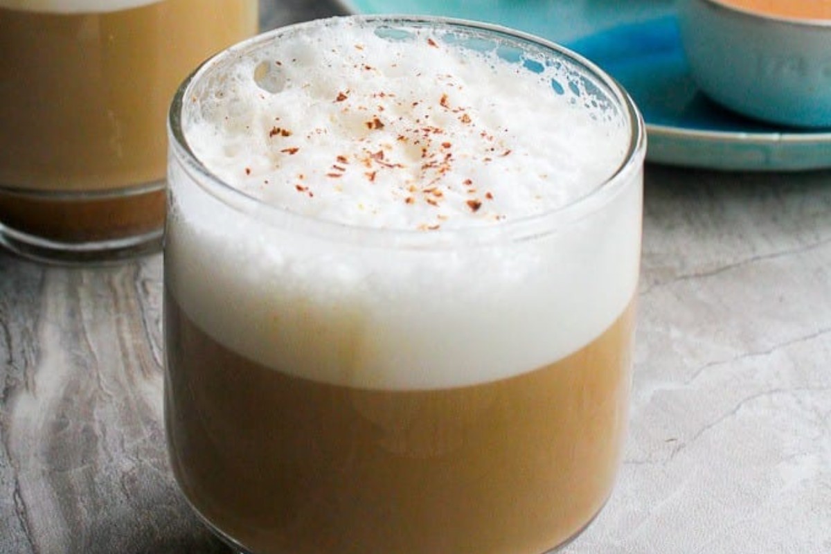 A glass filled with a pumpkin spice latte with a milk foam.