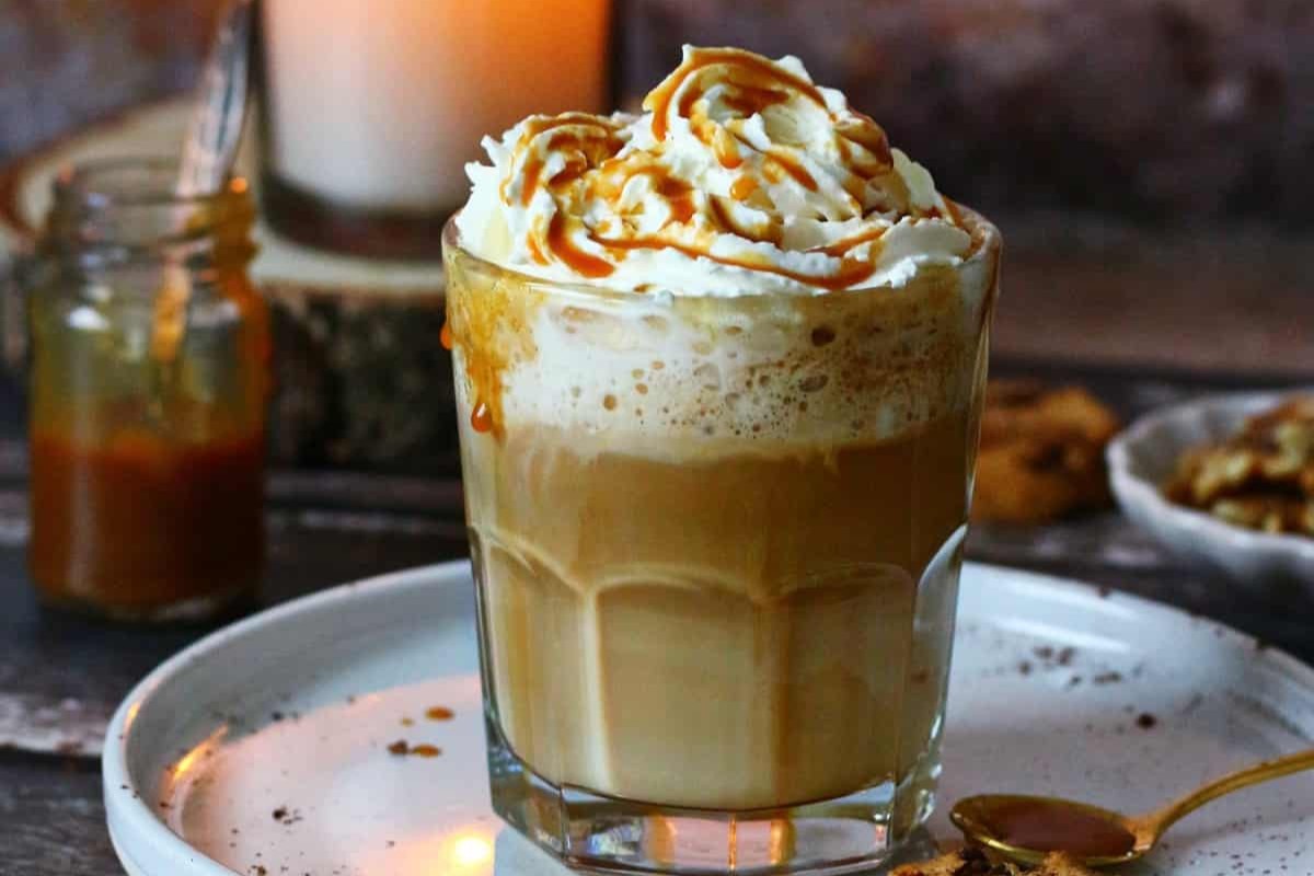 A glass filled with a caramel latte and whipped cream with a caramel drizzle.