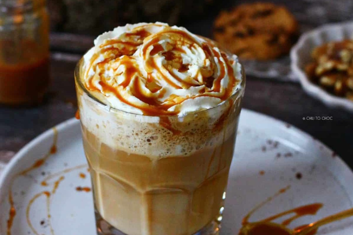A glass filled with a caramel latte and whipped cream with a caramel drizzle.