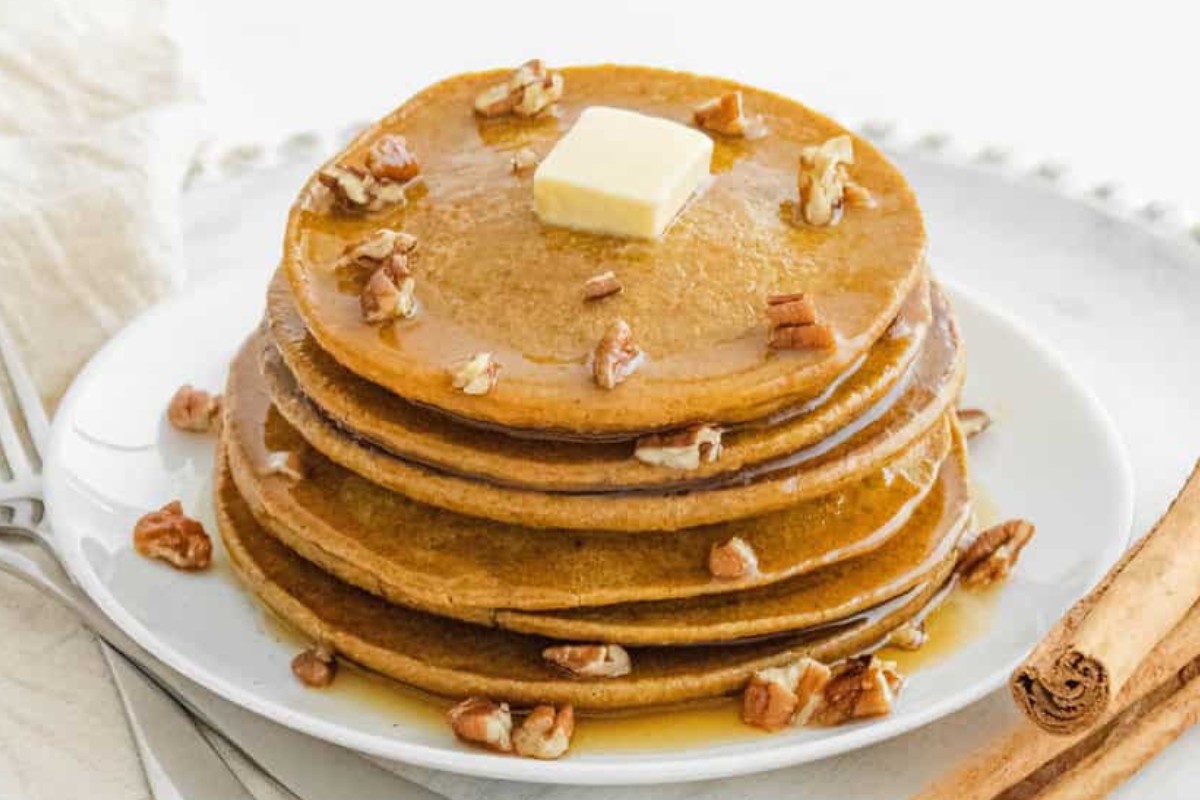 A plate with a stack of pumpkin pancakes with a dub of butter and cinnamon sticks.