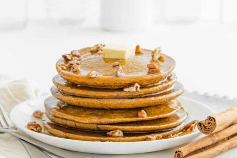 A plate with a stack of pumpkin pancakes with a dub of butter and cinnamon sticks.
