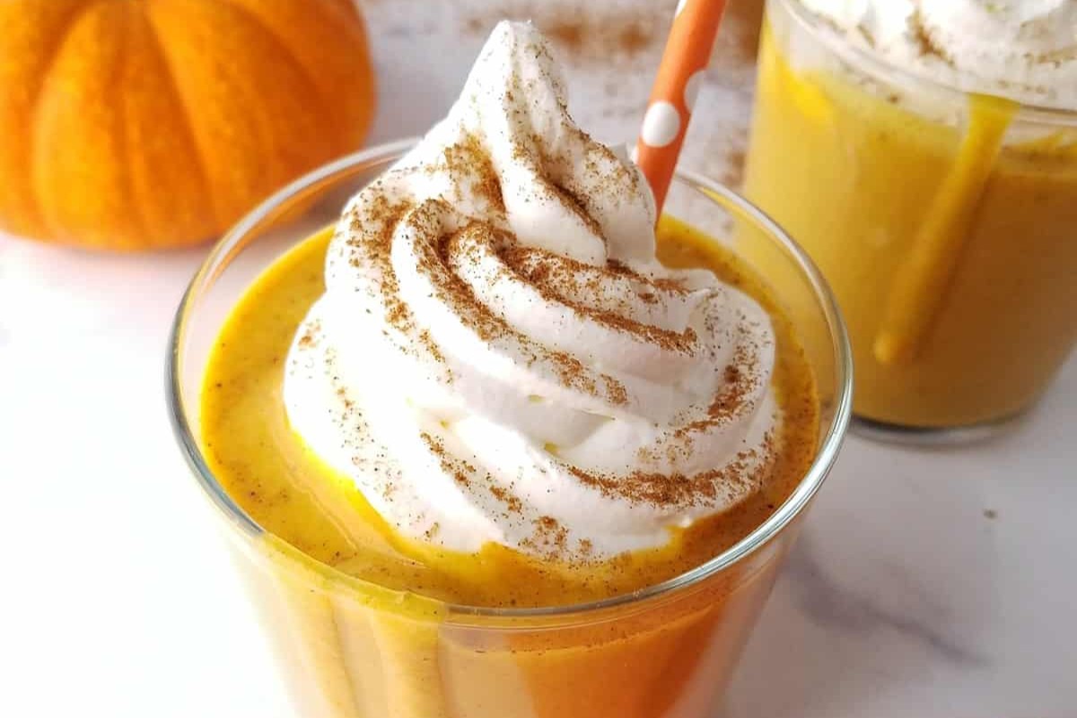 A glass filled with a pumpkin-flavored drink with a dollop of whipped cream and a straw.