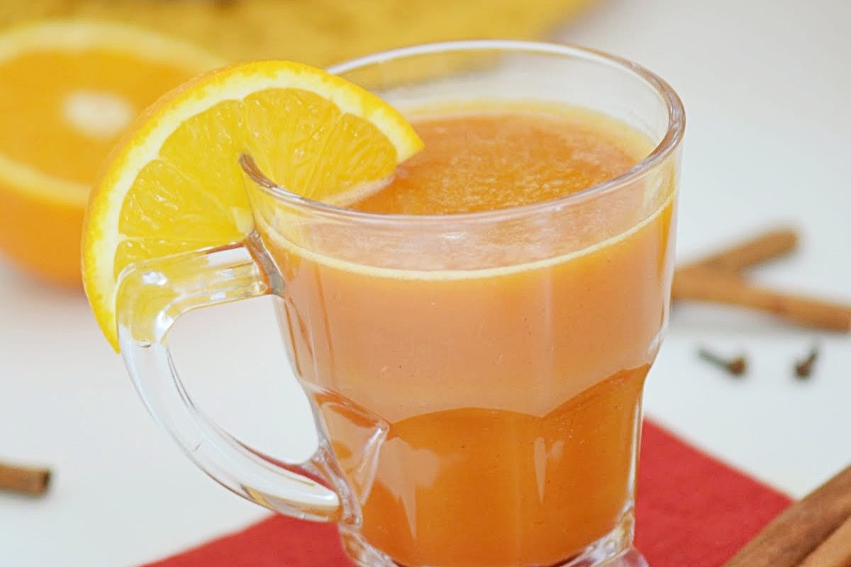 A glass filled with Pumpkin Cider with a orange wedge.