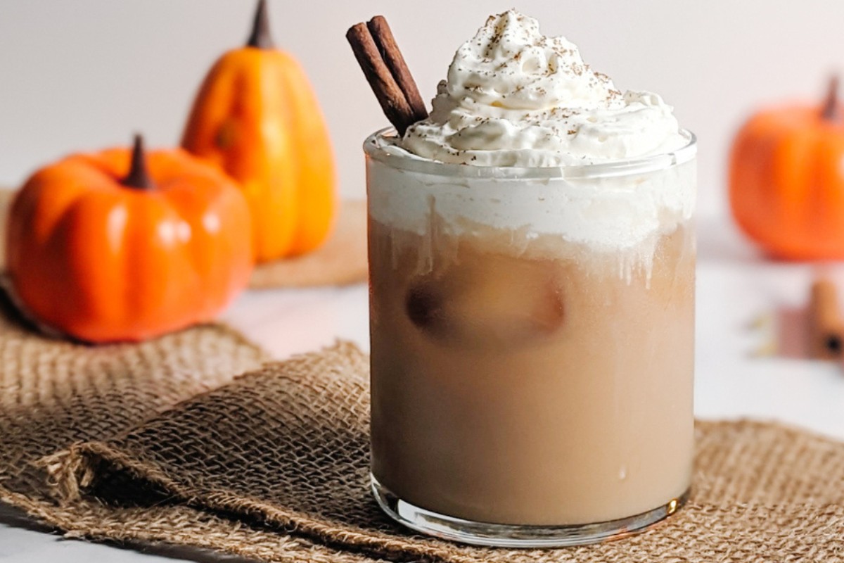 A glass is filled with a pumpkin spice chai latte with ceramic pumpkins in the background.