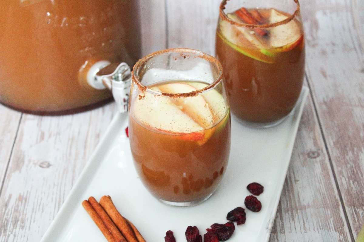 Two glasses filled with harvest Punch on a white platter with a jug of punch in the background.