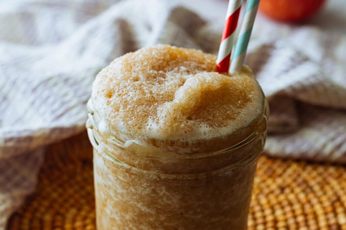 A glass jar filled with apple cider slushie with a striped straw.